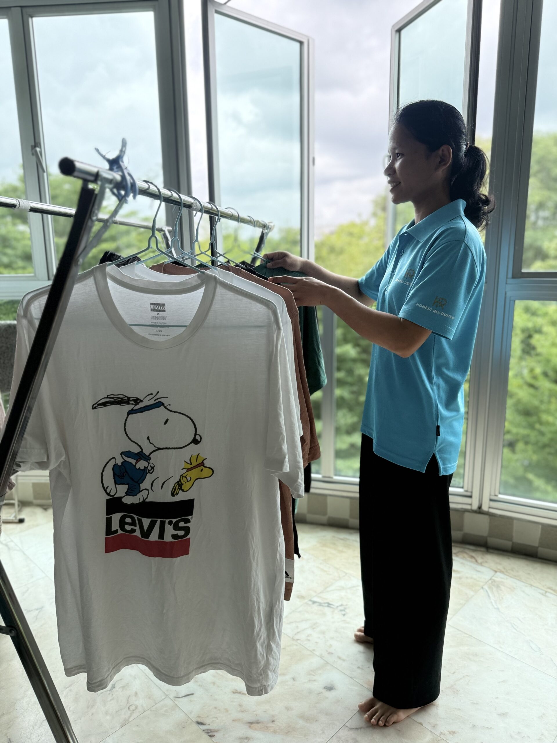 Honest Recruiter part-time cleaner hanging clothes on a drying rack beside a window during laundry service.