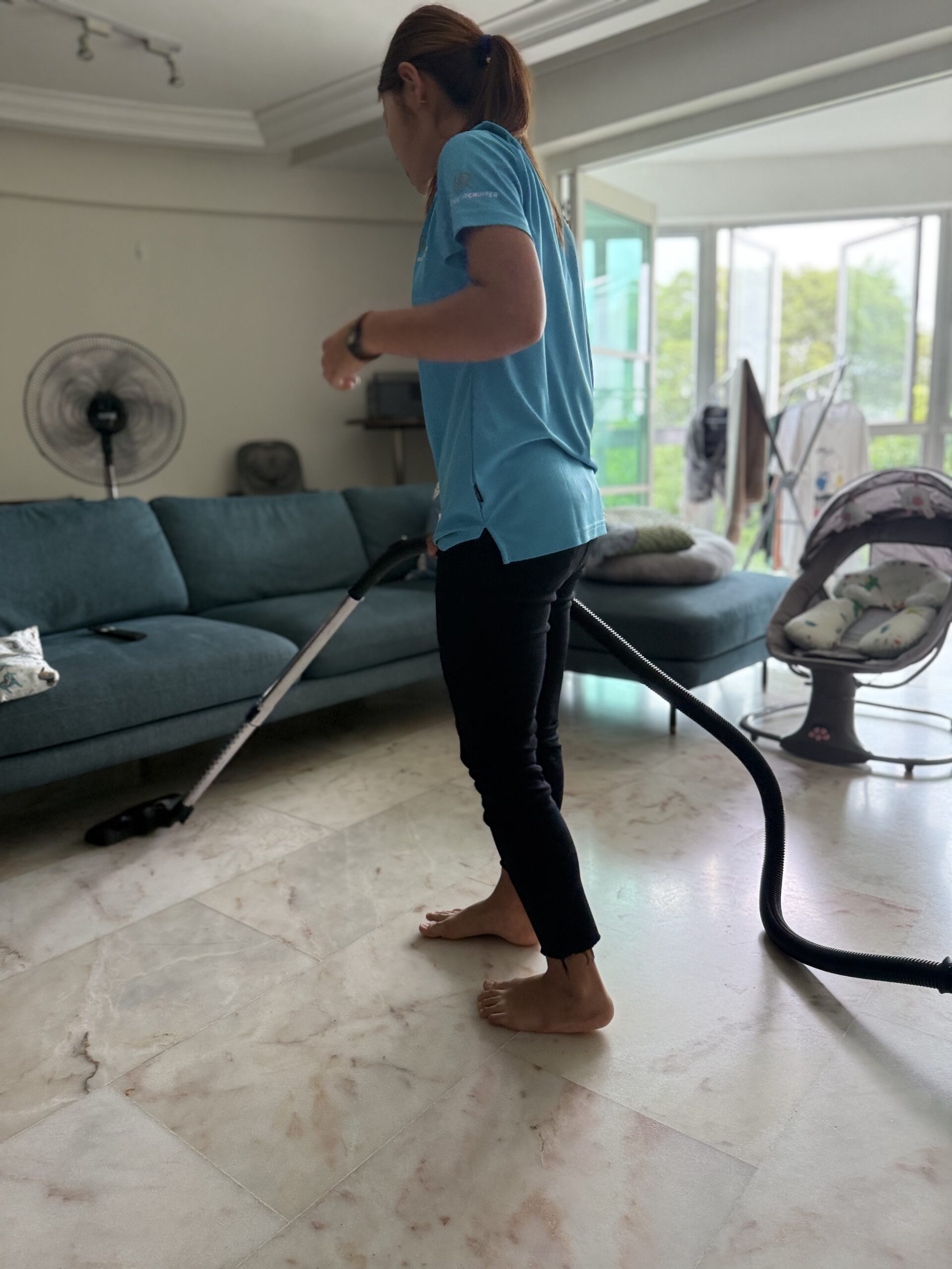 Honest Recruiter cleaner vacuuming a living room floor during part-time home support service in Singapore.